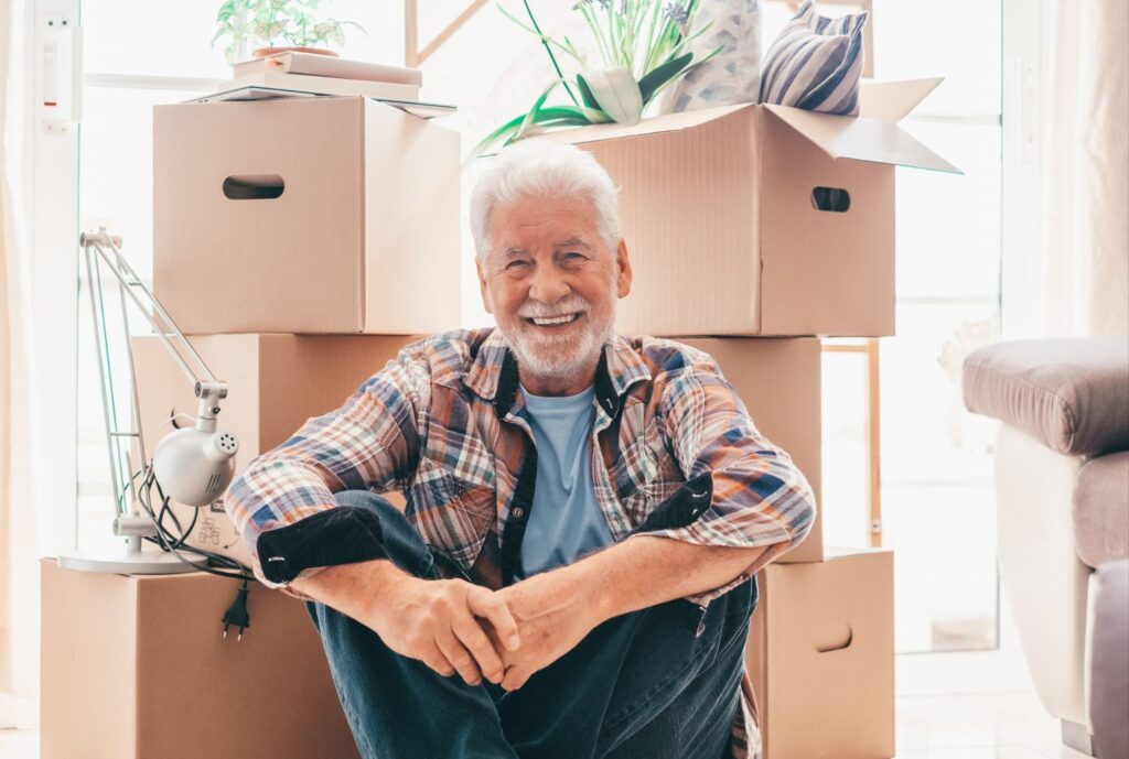 Senior man smiling while sitting next to boxes - Smooth Moves Texas senior relocation services