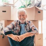 Senior man smiling while sitting next to boxes - Smooth Moves Texas senior relocation services